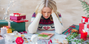 woman in holiday sweater, sitting a table with gifts around her, overwhelmed