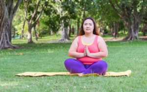 AAPI woman in pink tank top and yoga pants meditates outside in the park