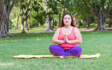 AAPI woman in pink tank top and yoga pants meditates outside in the park