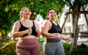 Two young AAPI women walking outside, wearing workout clothes and holding water bottles.