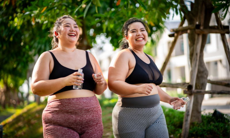 Two young AAPI women walking outside, wearing workout clothes and holding water bottles.