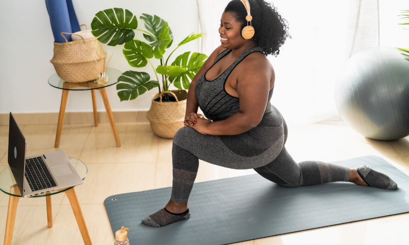 Young black woman does a workout on her yoga mat at home in front of her laptop