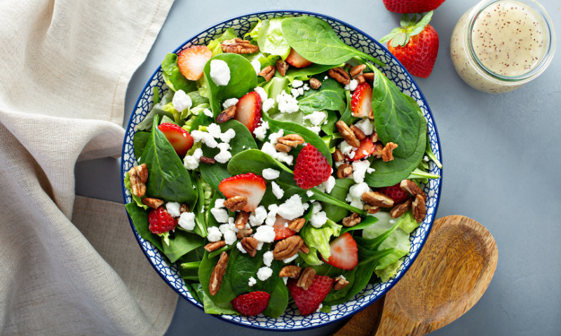 Bowl of strawberry spinach salad with nuts and goat cheese