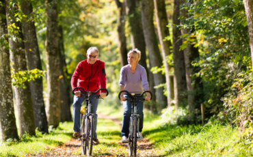 Older man and woman ride bikes together outside in the fall