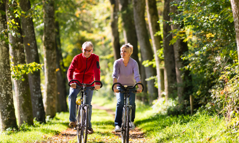 Older man and woman ride bikes together outside in the fall