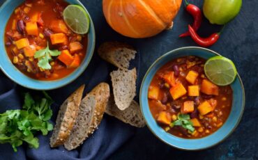 Image: Two bowls of pumpkin chili on a table next to fresh bread and fall table decor