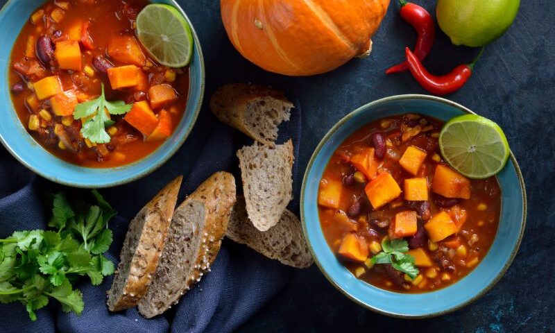 Image: Two bowls of pumpkin chili on a table next to fresh bread and fall table decor