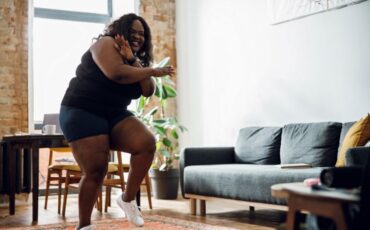 Image: Young black woman affected by obesity does a workout inside her living room during the day