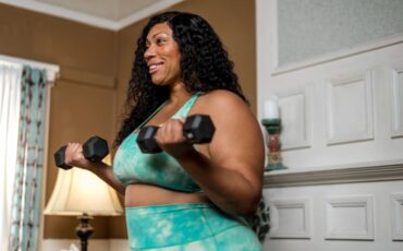 A black woman affected by obesity lifts weights in her bedroom at home