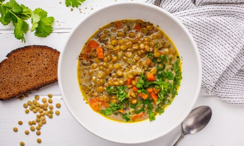 Bowl of lentil vegetable soup next to a slice of bread